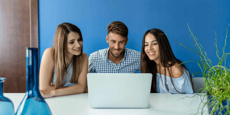 Três pessoas reunidas em frente ao computador conversando remotamente com um colega de trabalho talent as a service