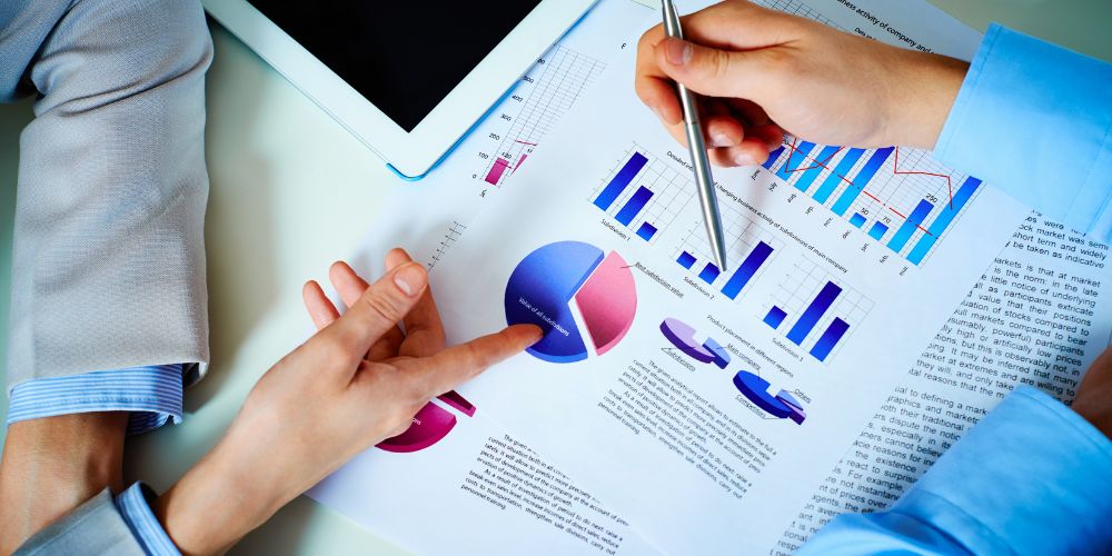 Pessoas analisando gráficos financeiros em papel, representando economia com IA no desenvolvimento de software.