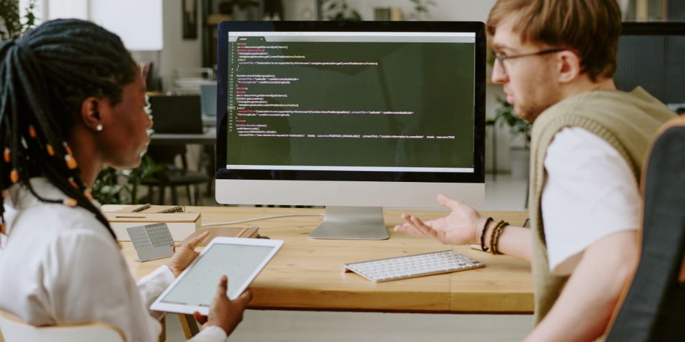 Profissionais de tecnologia analisando código juntos em frente a um monitor, discutindo como implementar squads cognitivos.