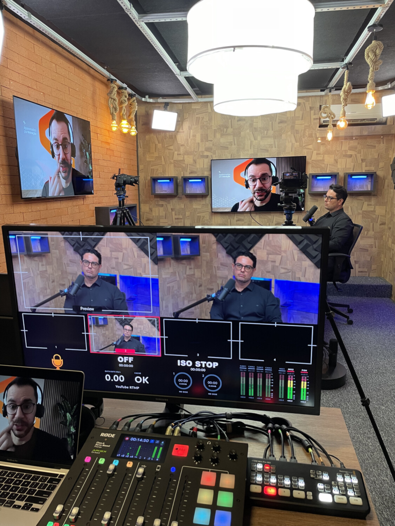 Bastidores da gravação do Vibbracast, com Leandro Oliveira no estúdio e Bruno Belini participando remotamente, enquanto câmeras e equipamentos de transmissão registram o episódio.