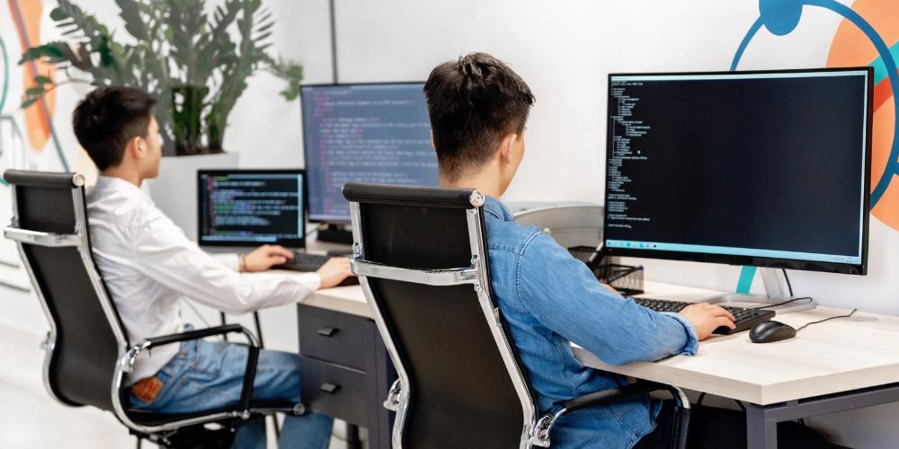 Dois desenvolvedores de software trabalhando em computadores com códigos de programação em um ambiente de engenharia de software.